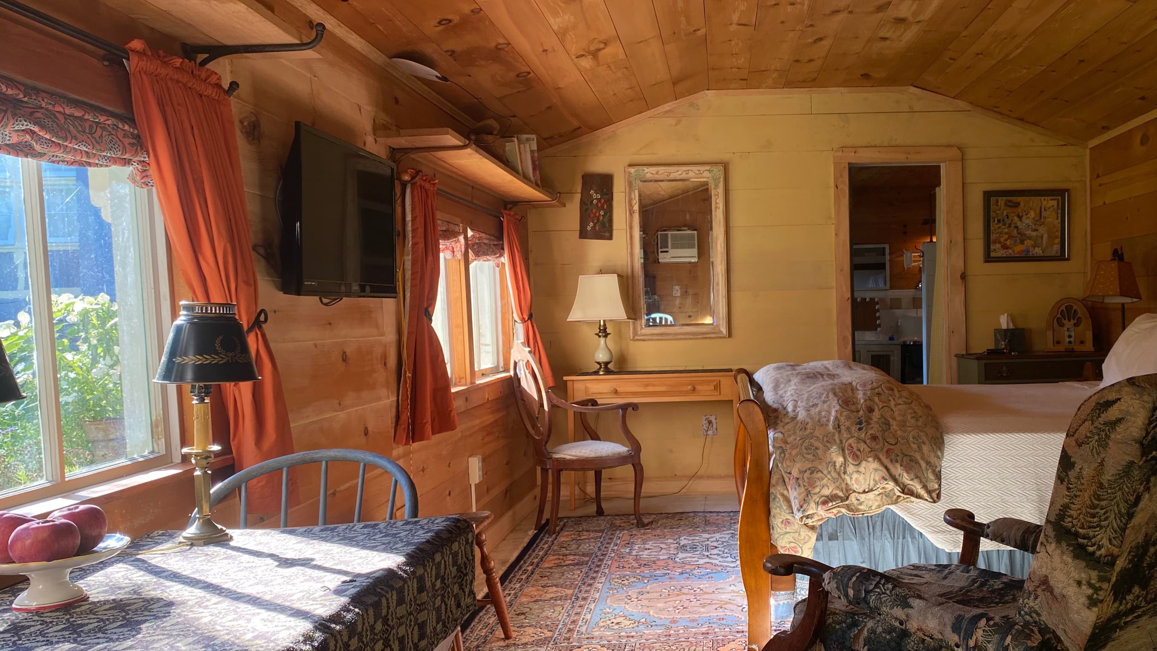 view of a beautifully made queen sized bed and four neatly placed pillows with a cozy gas fired stove and stovepipe and an old fashioned easy chair
