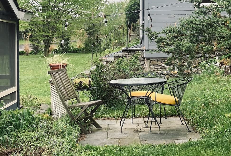 exterior photo of grey cottage with bright yellow door and 2 chairs with a table full of snacks and a round sign saying, welcome to the Fox Den