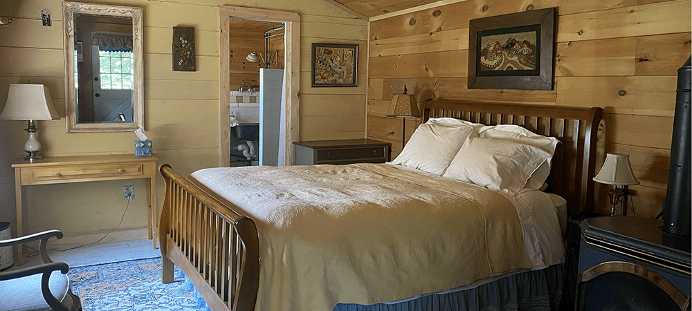 A cozy bedroom with wooden walls, a double bed, a nightstand, a mirror, and decorative paintings.