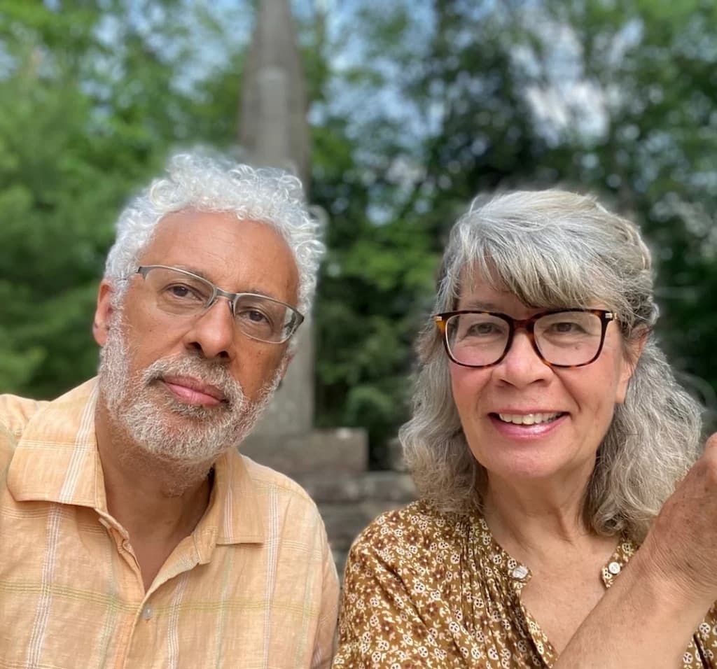 A close-up photo of a man and woman posing together outdoors with trees and a monument in the background.