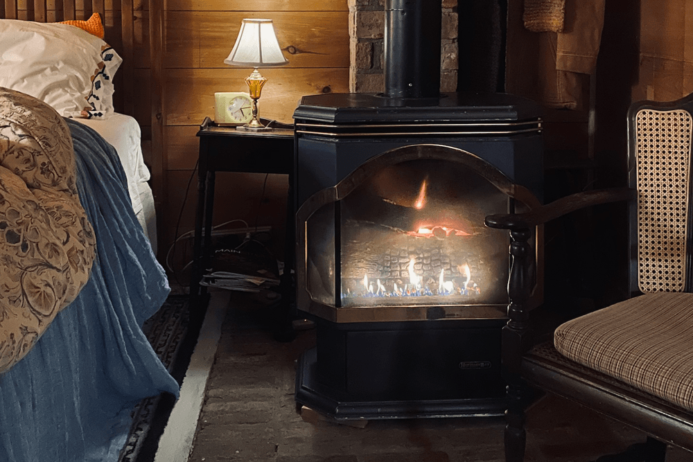 A cozy bedroom scene featuring a gas fireplace, a lamp on a nightstand, and a stylish chair.
