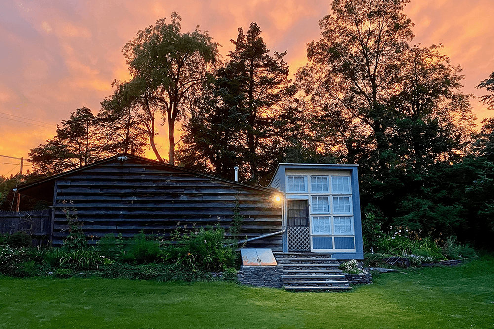 A rustic cabin surrounded by trees, illuminated by a vibrant sunset sky.